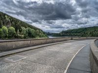 concrete walkway with trees and fenced in area on opposite sides of the road and one side of the road