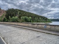 concrete walkway with trees and fenced in area on opposite sides of the road and one side of the road