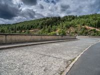 concrete walkway with trees and fenced in area on opposite sides of the road and one side of the road