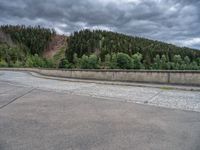 concrete walkway with trees and fenced in area on opposite sides of the road and one side of the road