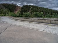 concrete walkway with trees and fenced in area on opposite sides of the road and one side of the road