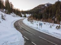 an empty road covered in snow on top of a mountain with mountains in the background