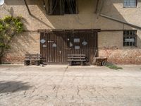 two benches sit in front of a wall covered with ivys and a door with signs