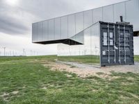 two buildings that are sitting in the grass outside of them with wind turbines behind them