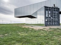 two buildings that are sitting in the grass outside of them with wind turbines behind them