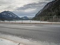 the mountains surrounding a lake are covered in snow as a man walks across it beside a fence