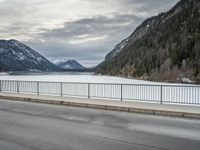 the mountains surrounding a lake are covered in snow as a man walks across it beside a fence