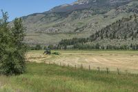 large green farm and a road surrounded by tall grass and mountains with trees lining the valley