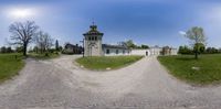 a large house with a tower sits in a grassy field with dirt roads that cross into the photo