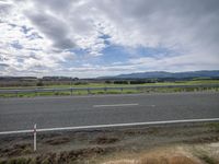 a highway with an empty street and grassy area in the distance and hills behind it