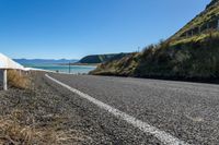 an empty rural highway next to a mountain range with blue sky in the background and some water on the ground