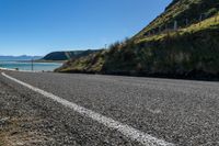 an empty rural highway next to a mountain range with blue sky in the background and some water on the ground