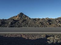 a motorcycle driving on a rural highway past a mountain of rock and gravel with blue sky in the background