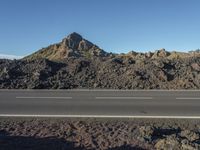 a motorcycle driving on a rural highway past a mountain of rock and gravel with blue sky in the background