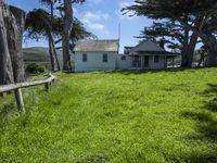 the home is in a grassy field by some trees and the road beside it runs along the property