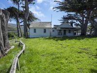 the home is in a grassy field by some trees and the road beside it runs along the property