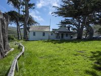 the home is in a grassy field by some trees and the road beside it runs along the property