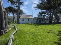 the home is in a grassy field by some trees and the road beside it runs along the property