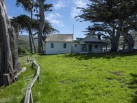 the home is in a grassy field by some trees and the road beside it runs along the property