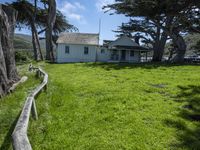 the home is in a grassy field by some trees and the road beside it runs along the property