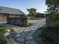 an open pathway in front of a building with a slate roof and stone walkway that leads to two entrances