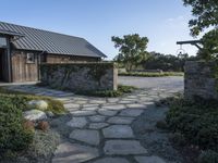 an open pathway in front of a building with a slate roof and stone walkway that leads to two entrances