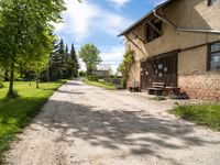 a dirt road leading to a building with a bench on the side and some trees