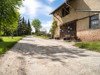 a dirt road leading to a building with a bench on the side and some trees