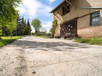 a dirt road leading to a building with a bench on the side and some trees