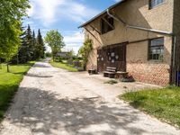 a dirt road leading to a building with a bench on the side and some trees