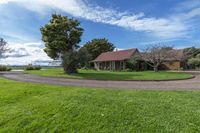 an outside shot of a house near a tree and grassy field with trees in the background