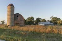 a tall barn on the side of a rural road, near the country road and tree line