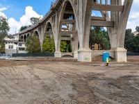 a construction site under the interstate bridge with several buildings below it and trees around the perimeter