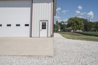 the side of a building with a motorcycle parked in front of it, in a gravel area in front of an open field