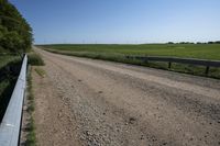 a single track bridge over a dirt road between green fields and bushes on both sides of a gravel road