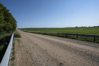a single track bridge over a dirt road between green fields and bushes on both sides of a gravel road