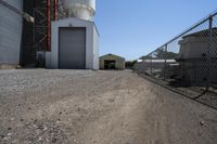 a farm is parked behind a chain link fence near a silo and warehouse building