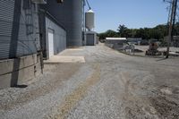 a gravel road in front of an industrial building and water tower with two silo on top