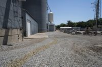 a gravel road in front of an industrial building and water tower with two silo on top