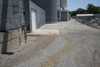 a gravel road in front of an industrial building and water tower with two silo on top