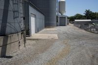 a gravel road in front of an industrial building and water tower with two silo on top