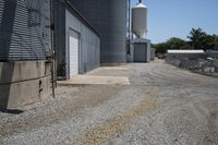 a gravel road in front of an industrial building and water tower with two silo on top