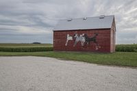 a building with a painting of horses on a red barn next to a field of corn