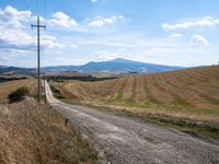 a dirt road leads to a field with mountains in the distance, there is no one in the photo