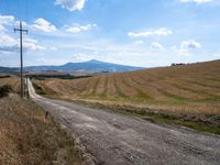 a dirt road leads to a field with mountains in the distance, there is no one in the photo