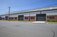 a large building with two garages with doors on it and a paved street lined by grass