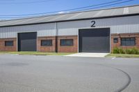 a large building with two garages with doors on it and a paved street lined by grass