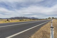 an open highway that is next to a dry plain with grass and bushes in the distance