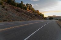 a person riding a motorcycle on a road at dusk with hills and bushes in the background