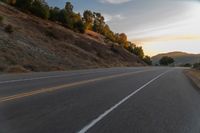 a person riding a motorcycle on a road at dusk with hills and bushes in the background